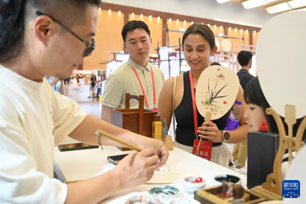 6月26日，美国青年在2024“鼓岭缘”中美青年交流周非遗展演暨青年集市开市活动上观看中国艺术家在扇面上作画。新华社记者 林善传 摄